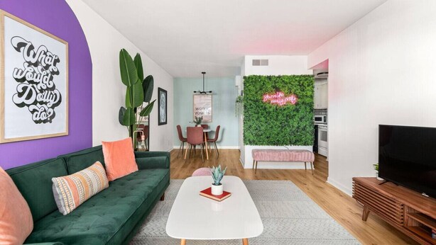 Un soggiorno moderno con un divano verde, un tavolino bianco e una TV su un mobile in legno.