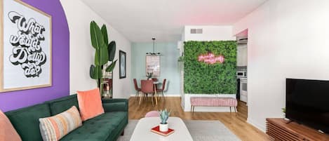 Ein modernes Wohnzimmer mit einem grünen Sofa, einem weißen Couchtisch und einem Fernseher auf einem Holzständer.