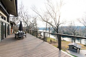 Eine Holzterrasse mit Gartenmöbeln, mit Blick auf einen Fluss und Bäume.