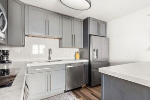 A modern kitchen with grey cabinets, stainless steel appliances, a marble countertop, and a wooden floor. - Best Location! Walk to Midtown Bars (Nashville)