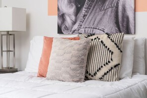 Ein Bett mit weißer Bettwäsche, eine Lampe und eine Wand mit Aufdruck eines Jeansjacks.