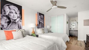 Ein modernes Schlafzimmer mit zwei Betten, einem Deckenventilator und einem sichtbaren Küchenbereich.