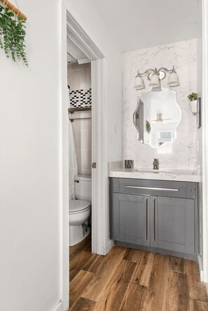A bathroom with a white toilet, grey cabinets, and a marble backsplash. - Best Location! Walk to Midtown Bars (Nashville)