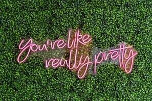 Ein Neonzeichen mit dem Text 'you're really pretty' vor einem grünen Blätterhintergrund.