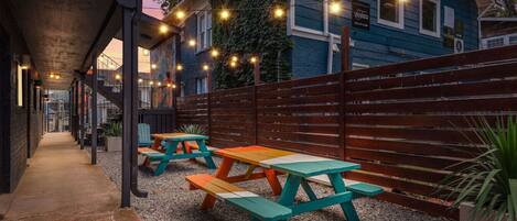 Ein Außenbereich mit einer Terrasse, Picknicktischen, Lichterketten und einem Holzzaun.