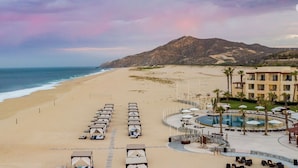 A beach resort with tents, a swimming pool, and a mountain in the background. - Pueblo Bonito Sunset Oceanview Junior Suite 🌅 Sleeps 4 | All-Inclusive (Cabo San Lucas)
