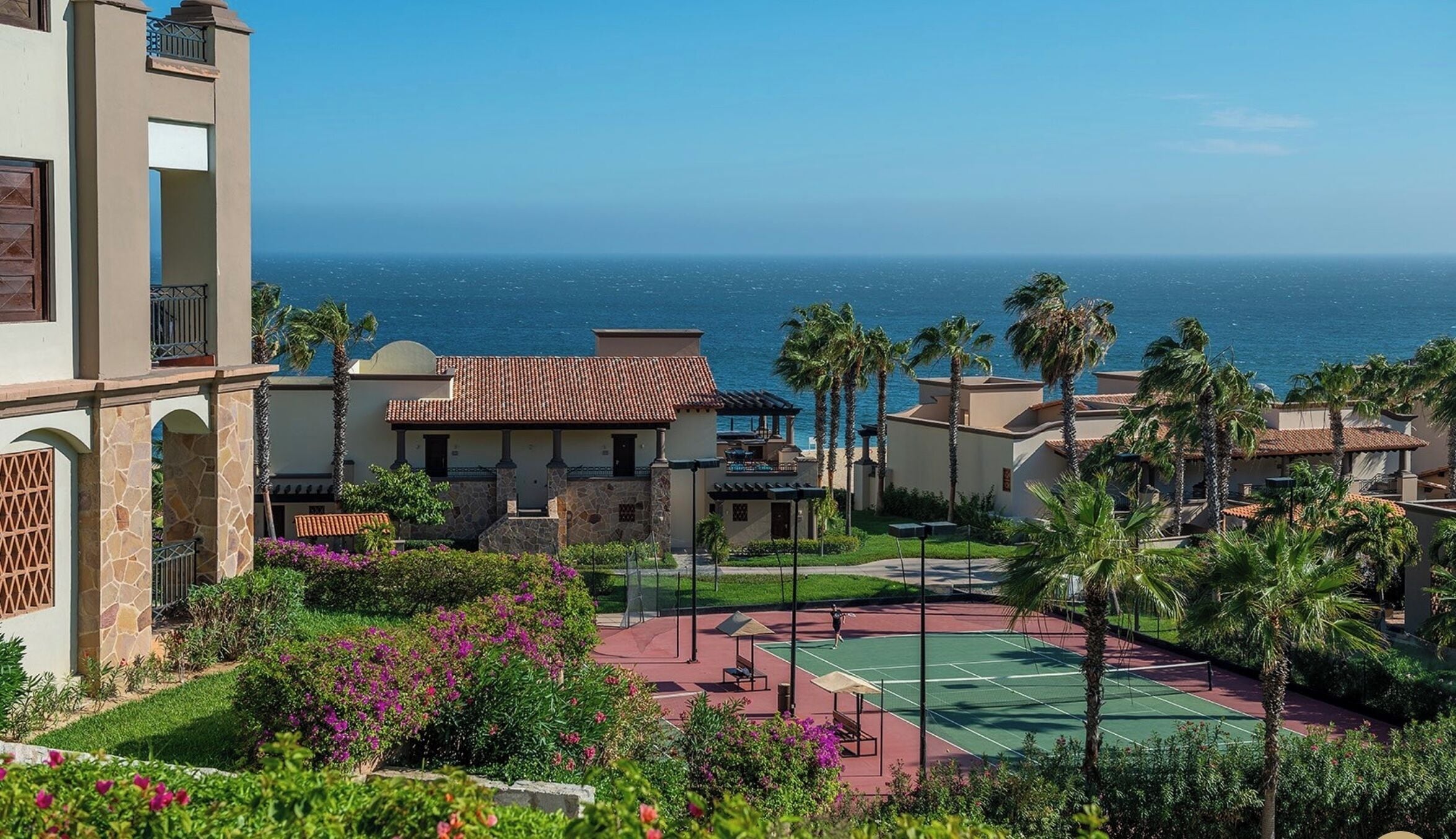 Ett semesterparadis med en tennisbana, palmer och utsikt över havet.