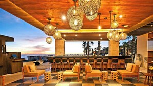 A bar area with wooden furniture, hanging lights, and a view of the beach. - Pueblo Bonito Sunset Oceanview Junior Suite 🌅 Sleeps 4 | All-Inclusive (Cabo San Lucas)