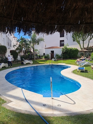 Una piscina con sillas de descanso, un área techada y un edificio al fondo.