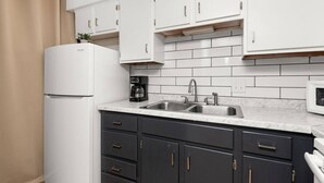 Una cucina con mobili bianchi, una macchina da caffè nera, un lavello e un forno a microonde.