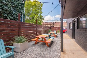 Un espace extérieur aménagé en terrasse, avec des tables et des chaises de pique-nique, un sol en gravier et une clôture en bois.