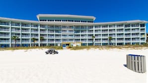 Een hotel met meerdere verdiepingen, balkons, uitzicht op het strand en een zandig voorgrondgebied.