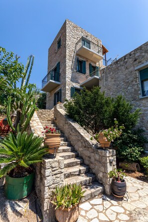 A stone building with a staircase leading to a balcony. There are potted plants and a large cactus visible. - Holiday Home 'Villa Oneiro' with Sea View, Wi-Fi and Air Conditioning (Στούπα)