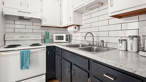 A modern kitchen with white cabinets, a stainless steel sink, a microwave, and a stove. - The Lyric - Music Row Right at Your Doorstep (Nashville)