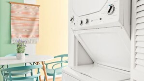 A room with a white washing machine, a table with chairs, and a wall with a patterned tapestry. - The Lyric - Music Row Right at Your Doorstep (Nashville)