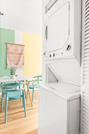 Ein Zimmer mit einer weißen Waschmaschine, einem Tisch mit Stühlen und einer Wand mit einem gemusterten Wandteppich.