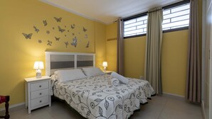 Une chambre à coucher avec un lit, des tables de chevet, une lampe, une fenêtre avec des rideaux et des autocollants décoratifs représentant des papillons sur les murs.