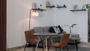 En moderne stue med en grå sofa, to brune lænestole, et lille rundt bord og en pendel. Væggene har reoler med dekorative genstande, og der står en gulvlampe.