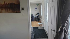 A hallway with a door, a small table, a chair, a radiator, and a plant. - Rimouski te espera ! (Rimouki)