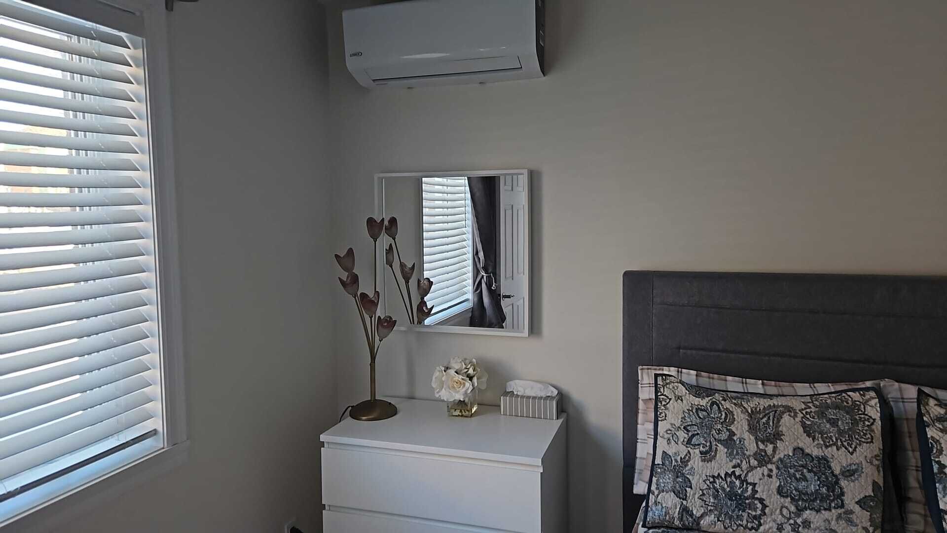 Une chambre à coucher avec un lit, une commode, un miroir et une fenêtre avec des stores.