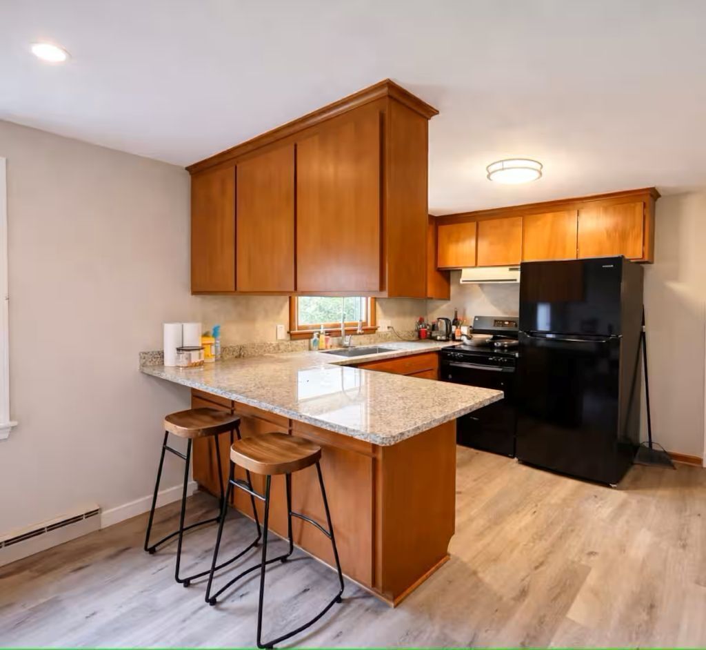 A kitchen with wooden cabinets, a black refrigerator, and a granite countertop.