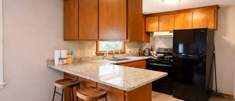 A kitchen with wooden cabinets, a black refrigerator, and a granite countertop.