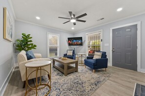 Ein Wohnzimmer mit Deckenventilator, Fernseher, zwei Sofas, einem Couchtisch und einer Pflanze.