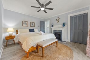 Un dormitorio con cama, mesita de noche, banca, ventilador de techo, chimenea y varios armarios.