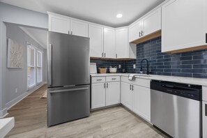 Eine moderne Küche mit weißen Schränken, einem Edelstahlkühlschrank, einem Geschirrspüler und einer blau gefliesten Spritzschutzwand.