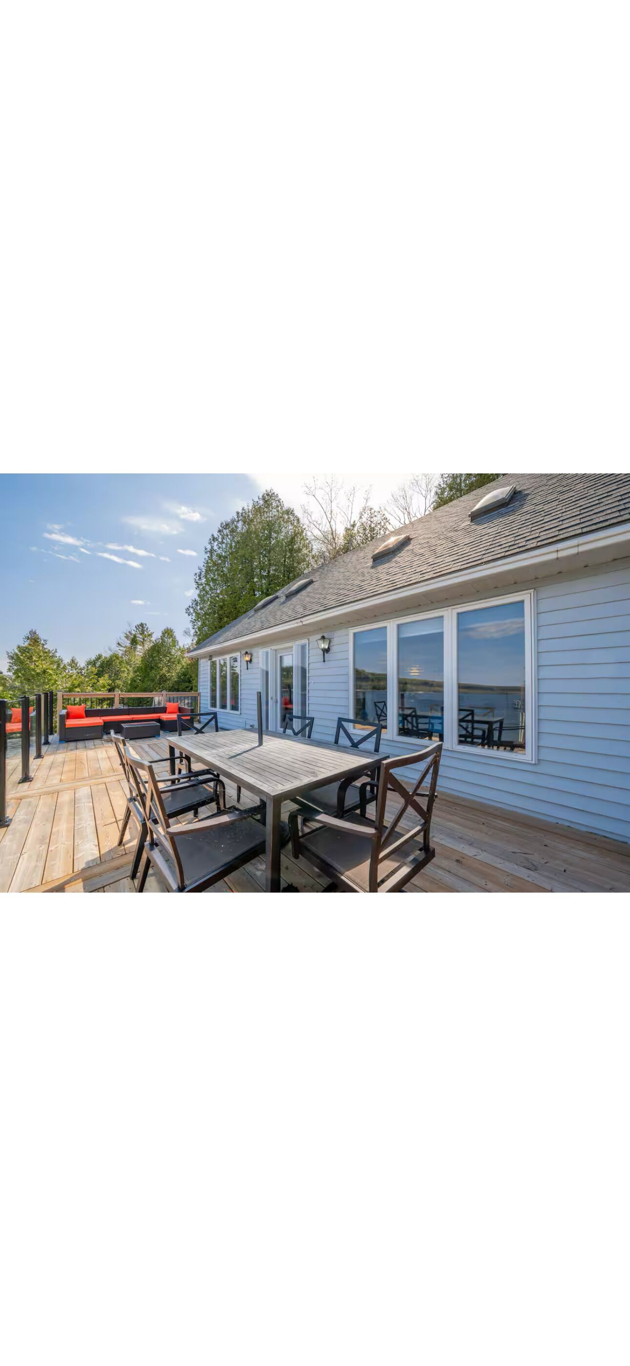 Une terrasse en bois avec une table et des chaises, un espace salon couvert et un bâtiment doté de grandes fenêtres.