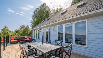 Une terrasse en bois avec une table et des chaises, un espace salon couvert et un bâtiment doté de grandes fenêtres.