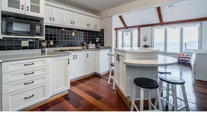 Cocina con alacenas blancas, microondas y una zona de comedor con taburetes.