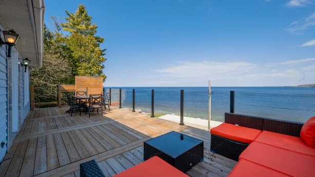 Una terraza de madera con mobiliario exterior, una mesa y vista al océano.