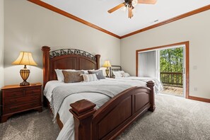 Ein Schlafzimmer mit einem hölzernen Bett, zwei Nachttischen mit Lampen, einem Deckenventilator und Blick durch eine Glastür auf eine Terrassenfläche.