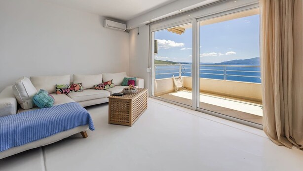 Ein Zimmer mit einer Couch, einem kleinen Tisch und Meerblick durch große Schiebetüren.