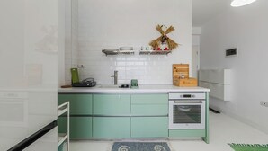 Eine Küche mit weiß gefliestem Fliesenspiegel, grünen Schränken, einem eingebauten Backofen und einem kleinen Regal mit Dekoration.
