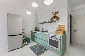 A kitchen with a refrigerator, oven, and a shelf with items. - Sunkissed Apartment | 1BR Amazing Views by the Sea by PikHost (Sarandë)