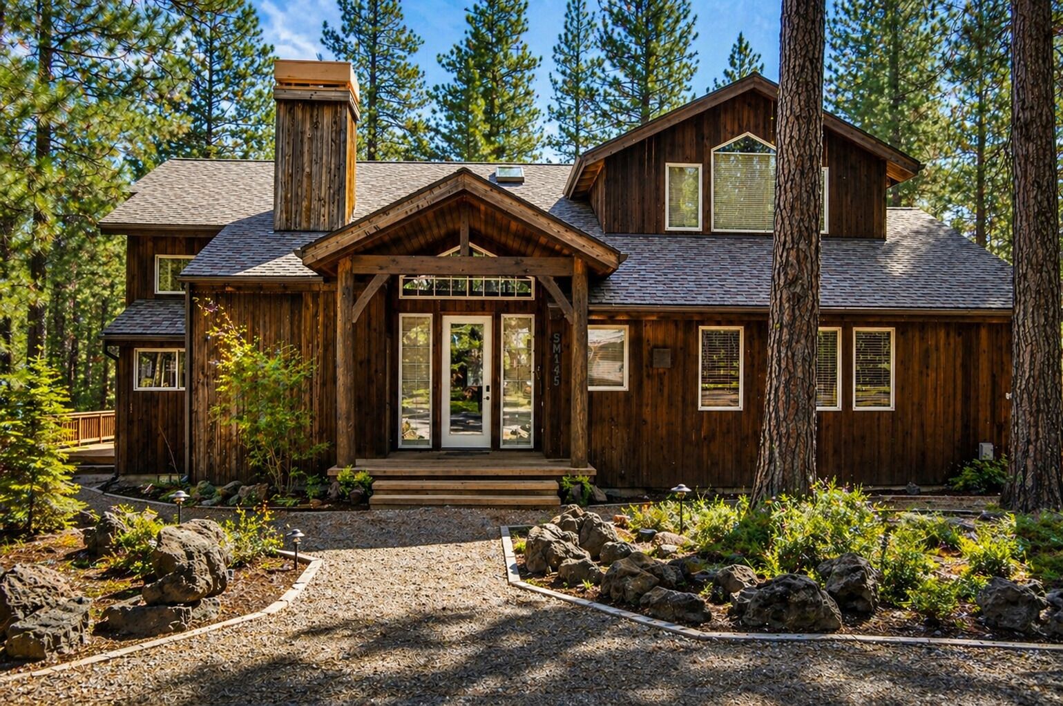 Rustic mountain cabin nestled among towering pines with natural stone landscaping and wooden architecture.