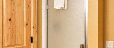 A wooden door, a glass shower enclosure, and a white towel hanging on the shower door handle.