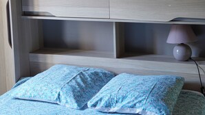 A bed with a floral-patterned bedspread and two pillows, a bedside lamp, and a wooden headboard with built-in shelves.