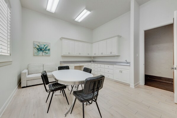 A modern kitchen with white cabinets, a dining table with chairs, and a light-colored floor.