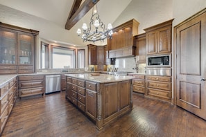 A spacious kitchen with wooden cabinets, a central island, a stainless steel microwave, and a chandelier.