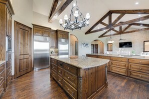 A spacious kitchen with wooden cabinetry, a large island, stainless steel appliances, and a vaulted ceiling with exposed beams.