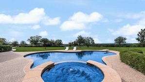 Ein Pool mit einem runden Whirlpool, umgeben von einem angelegten Garten und blauem Himmel.