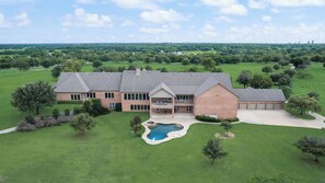 A large brick house with a pool, surrounded by a well-maintained lawn and trees.