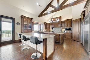 A spacious kitchen with a large island, wooden cabinets, stainless steel appliances, and a view to the outside.