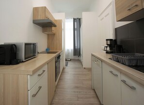 Eine schmale Küche mit Holzausstattung, einer Mikrowelle, einer Kaffeemaschine und einem Geschirrspüler.