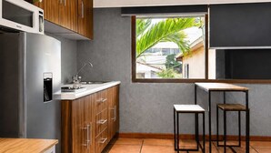 A compact kitchen with wooden cabinets, a built-in microwave, a sink, and a window with a view of greenery. - suite privada, zona consulado (Zapopan)