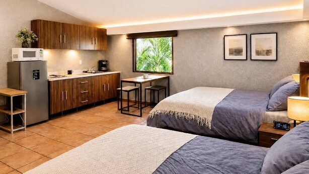 A compact hotel room with a kitchenette, two beds, a small dining table, and a window with a view of greenery. - suite privada, zona consulado (Zapopan)
