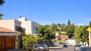 A residential street with parked cars, houses with tiled roofs, and greenery. - suite privada, zona consulado (Zapopan)